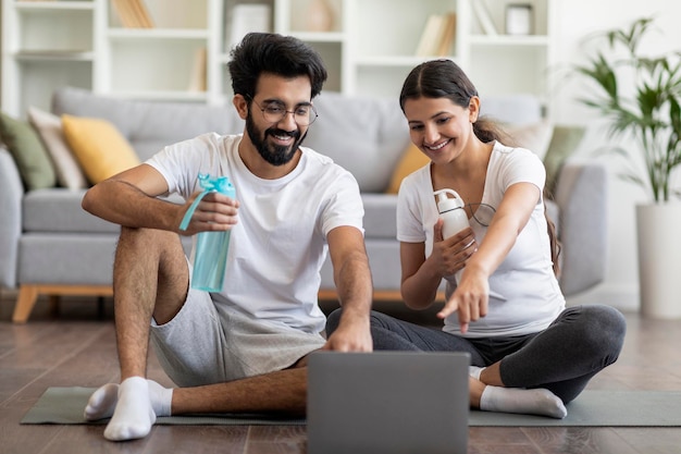 Feliz joven pareja india eligiendo tutoriales en línea en una computadora portátil para entrenar en casa