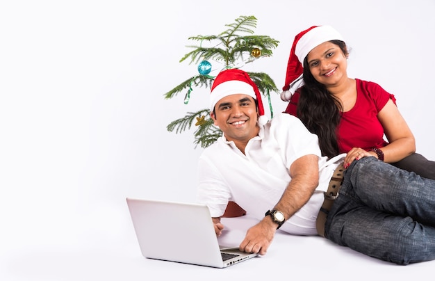 Feliz y joven pareja india en el sofá usando la computadora portátil mientras celebra la Navidad