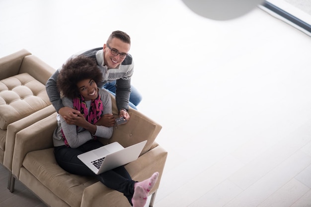 Feliz joven pareja multiétnica comprando en línea a través de una computadora portátil usando una tarjeta de crédito en casa