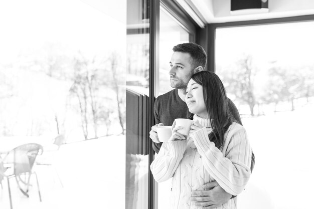 feliz joven pareja multiétnica disfrutando del café matutino junto a la ventana en el frío día de invierno en casa