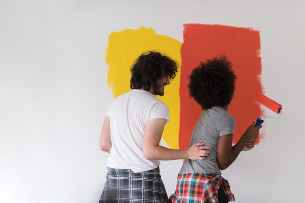 feliz joven pareja multiétnica pintando la pared interior de la nueva casa