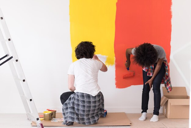 feliz joven pareja multiétnica pintando la pared interior de la nueva casa