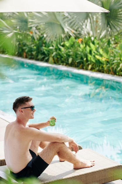 Feliz joven pasar un día soleado en la piscina y beber un cóctel frío