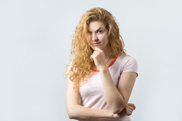 Feliz joven pelirroja caucásica con camisa de verano mira a un lado con expresión pensativa y está considerando un plan de acción adicional