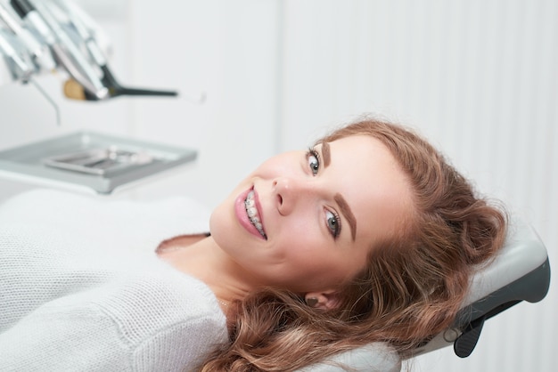 Feliz joven pelirroja con tirantes sonriendo sentado en un sillón dental