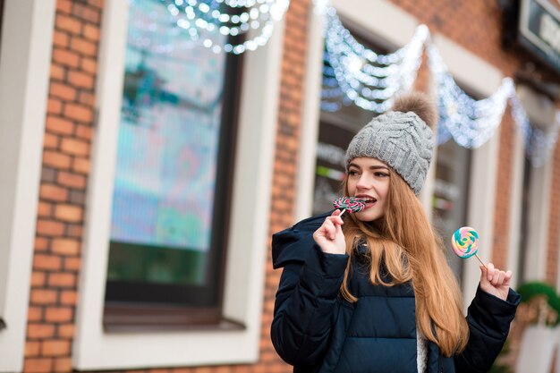 Feliz joven pelirroja vistiendo gorro de punto gris y muerde dulces navideños