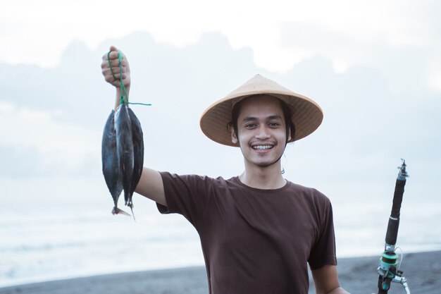 Feliz joven pescador en la playa sosteniendo su captura de peces y espectáculos