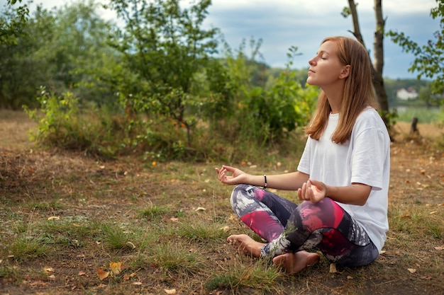 Feliz joven de pie en pose de yoga sobre la hierba en el parque