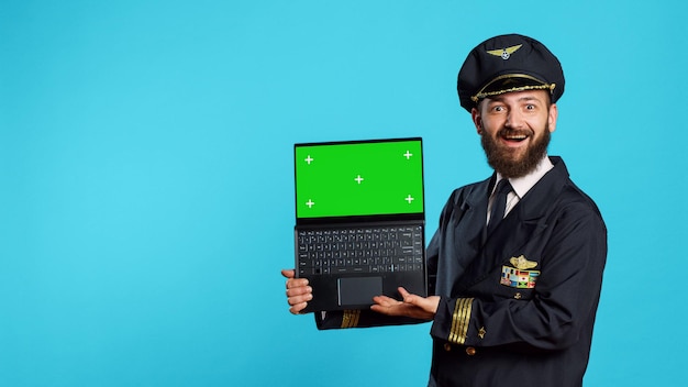 Feliz joven piloto sosteniendo una computadora portátil con pantalla verde, usando una pantalla aislada con llave de croma en una computadora portátil. Capitán de la tripulación aérea en uniforme mirando la plantilla de maqueta en blanco y el espacio de copia.