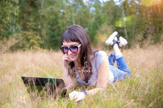 Feliz joven con un portátil en un césped soleado freelancer trabaja en la naturaleza estudiantil de forma remota