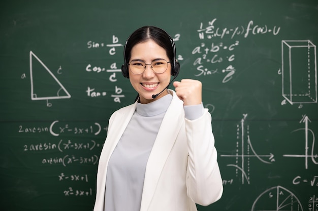 Feliz joven profesora asiática mostrando una videoconferencia de signos de pelea de puños con una estudiante mirando la cámara Profesora entrenando las matemáticas en el curso en línea de la pizarra del aula