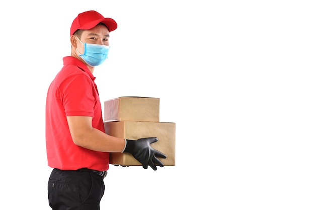 Feliz joven repartidor asiático en uniforme rojo, mascarilla médica, guantes protectores llevan caja de cartón