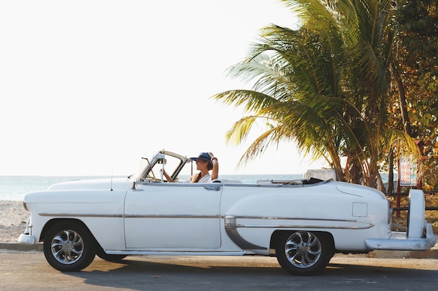 Feliz joven y retro coche convertible junto a la playa en la ciudad de Varadero