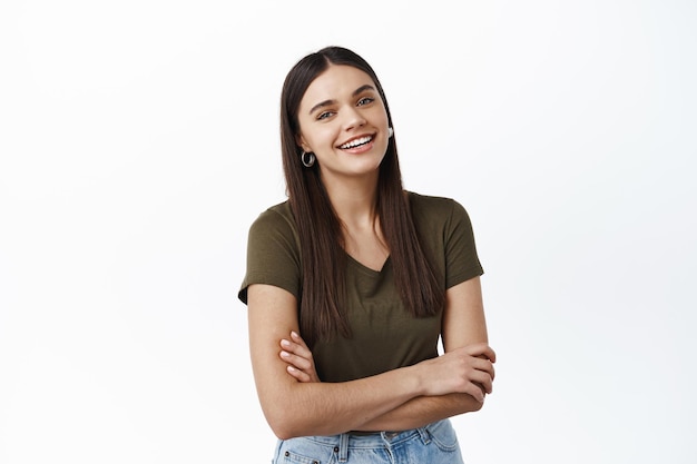 Feliz joven riendo y de pie casualmente en camiseta, tomados de las manos cruzadas sobre el pecho, mirando al frente naturalmente