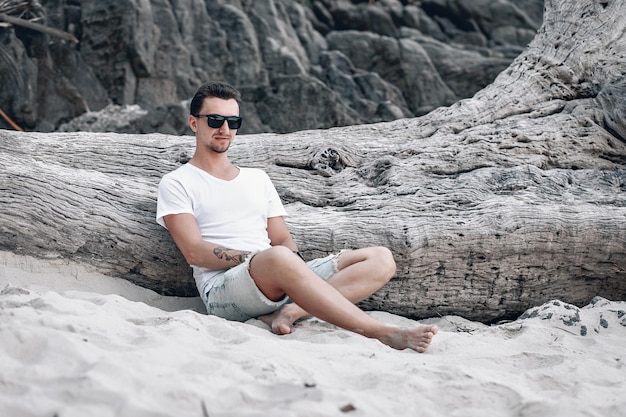 Feliz joven romántico con ropa blanca de verano posando en la cámara sentada en la arena