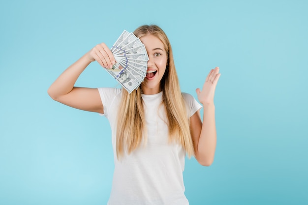 Feliz joven rubia con dinero en dólares en la mano aislada sobre azul