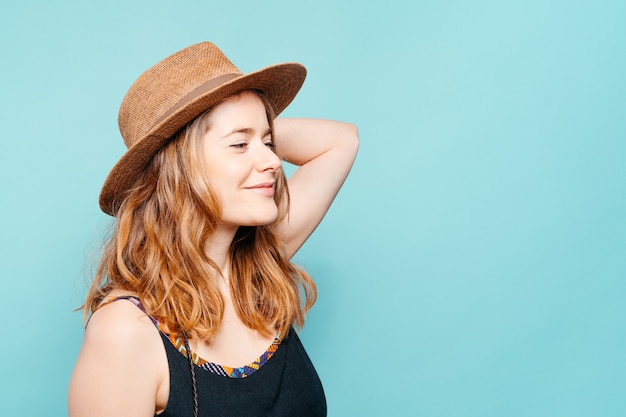 Feliz joven rubia mirando hacia el lado con un sombrero de paja sobre un fondo azul.