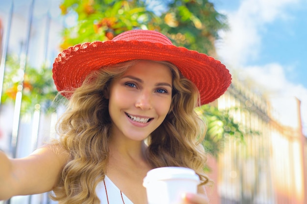 Feliz joven rubia sonriendo ampliamente haciendo autorretrato en su dispositivo al aire libre