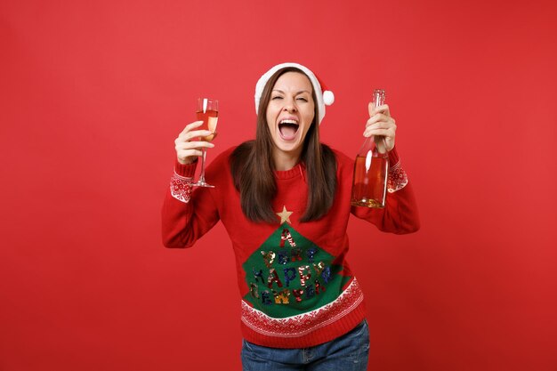 Feliz joven Santa con sombrero de Navidad gritando, sosteniendo una botella de champán aislado sobre fondo rojo brillante. Feliz año nuevo 2019 celebración concepto de fiesta navideña. Simulacros de espacio de copia.