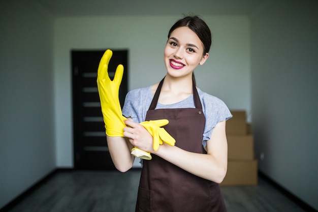 Feliz joven señora de la limpieza poniéndose guantes de goma, preparándose para la limpieza de primavera