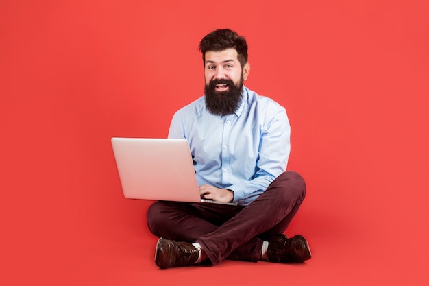 Feliz joven sentado en el suelo con y usando laptop