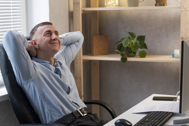 Feliz joven en sillón de cuero en su oficina. El trabajador de oficina consiguió un ascenso. Director de la empresa feliz descansando en su oficina.