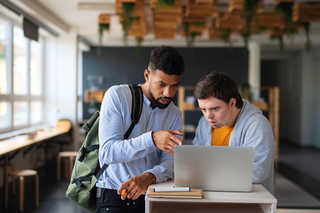 Feliz joven con síndrome de Down y su tutor usando lapotp en el interior de la escuela