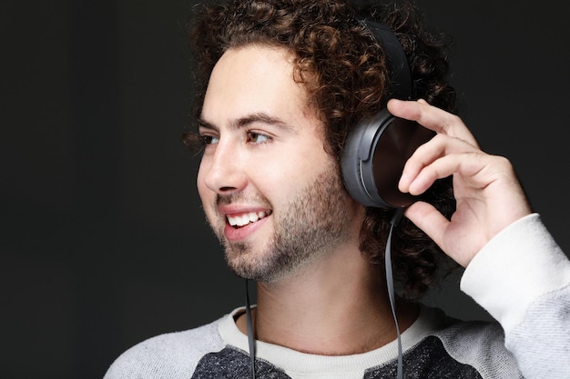 Feliz joven sonriendo escuchando música en auriculares sobre fondo gris