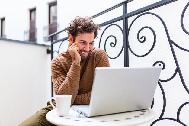 Feliz joven sonriendo, mientras trabaja en su computadora portátil para hacer todos sus negocios temprano en la mañana con su taza de café