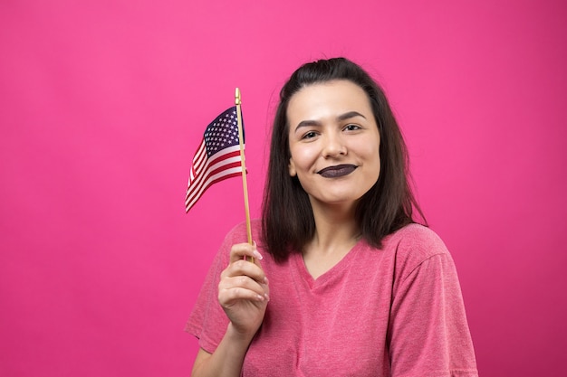 Feliz joven sosteniendo la bandera americana contra un fondo de color rosa studio