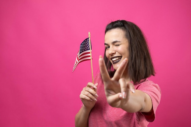 Feliz joven sosteniendo la bandera americana contra un fondo de color rosa studio