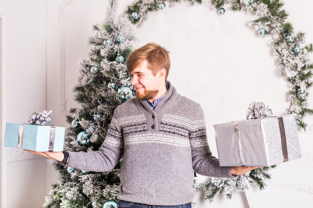 Feliz joven sosteniendo dos caja de regalo sobre fondo de árbol de Navidad.