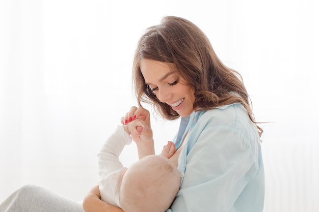 Feliz joven sosteniendo en las manos a su niño pequeño. Madre amamantando y abrazando a su bebé