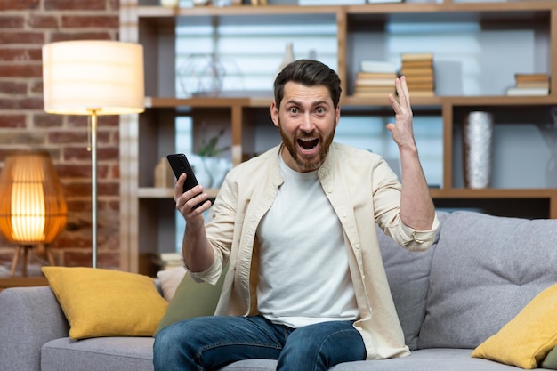 Feliz joven sosteniendo el teléfono en la mano feliz y celebrando mirando y gritando a la cámara. Recibió buenos mensajes de noticias, ganó la apuesta de lotería en el juego.