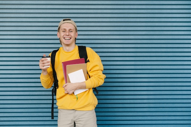 Feliz joven sostiene un libro y una taza de café en las manos