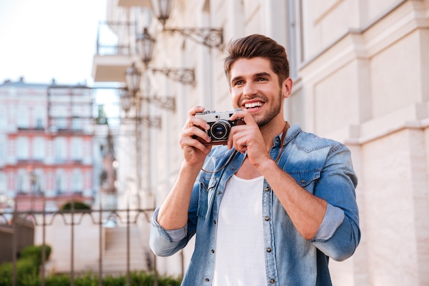 Feliz joven tomando fotografías con cámara de fotos vintage en la calle