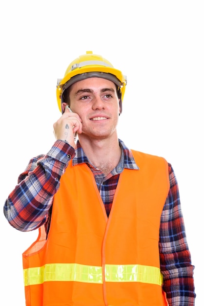 Feliz joven trabajador de la construcción pensando mientras habla por teléfono