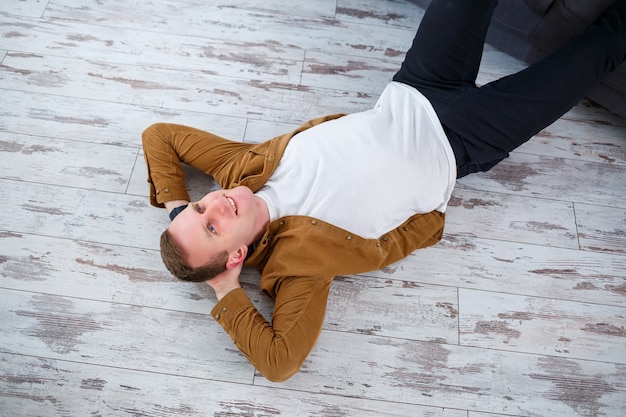 Foto feliz joven tumbado en el suelo cerca del sofá de la sala de estar y descansando