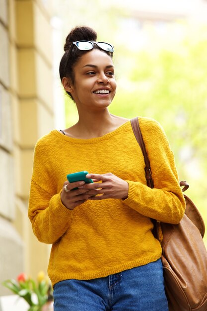 Feliz joven urbana caminando con teléfono móvil