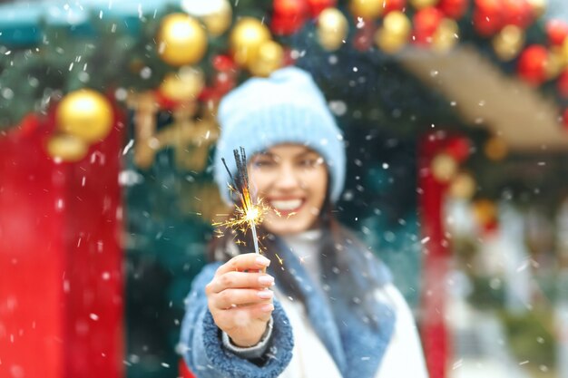 Feliz joven viste abrigo azul disfrutando de las vacaciones con luces de bengala durante las nevadas