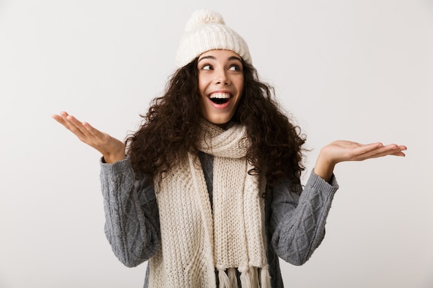 Feliz joven vistiendo ropa de invierno que se encuentran aisladas sobre la pared blanca, presentando espacio de copia