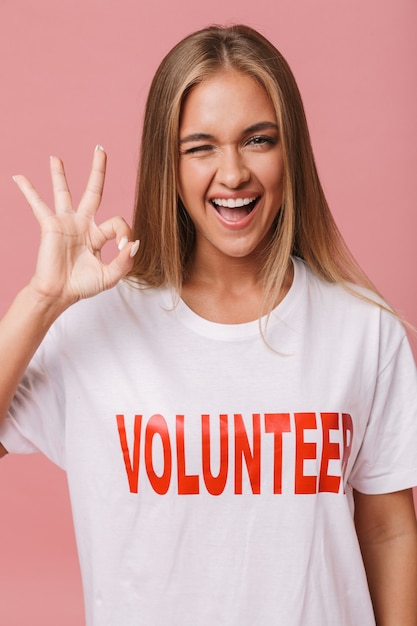 Feliz joven voluntaria que se encuentran aisladas, mostrando gesto ok, guiñando un ojo