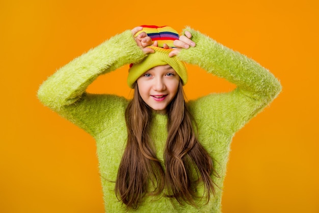 Feliz jovencita en suéter verde y sombrero de punto multicolor sobre un fondo amarillo