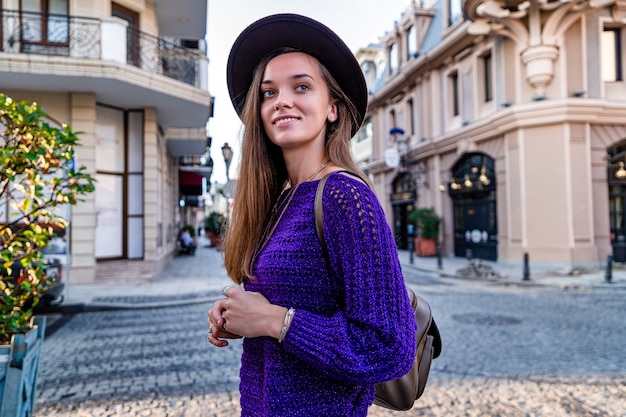 Feliz linda atractiva joven morena con sombrero con el pelo largo y suéter de punto durante caminar por la ciudad