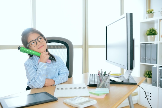 feliz linda empresária segurando a caneta grande sonhando acordado pensando o futuro da empresa planejando na mesa do computador no escritório.