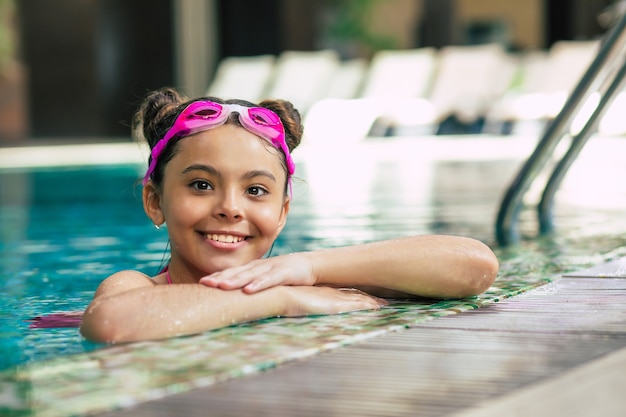 Feliz linda garotinha sorridente de óculos e maiô na piscina se diverte durante as férias ou aulas de natação.