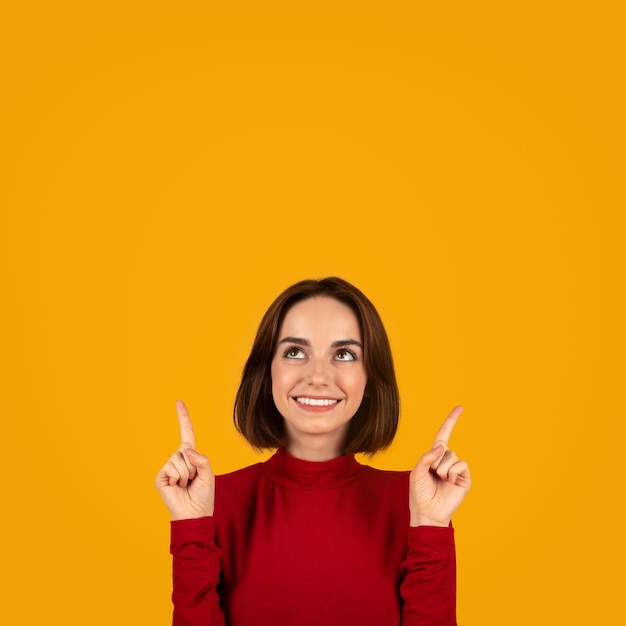 Foto feliz linda jovem em vermelho apontando para o espaço vazio