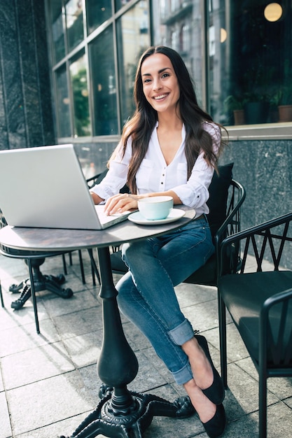 Feliz linda jovem empresária trabalhando no laptop no café de rua ao ar livre