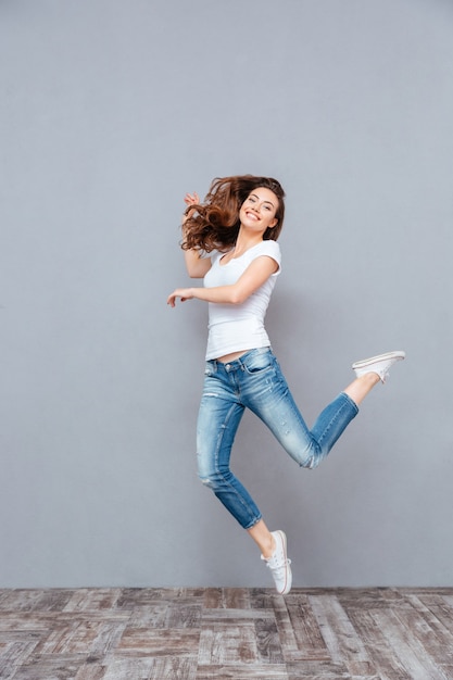 Feliz linda joven en camiseta blanca y jeans saltando