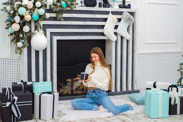 Feliz linda joven celebrando la Navidad en casa junto a la chimenea con regalos